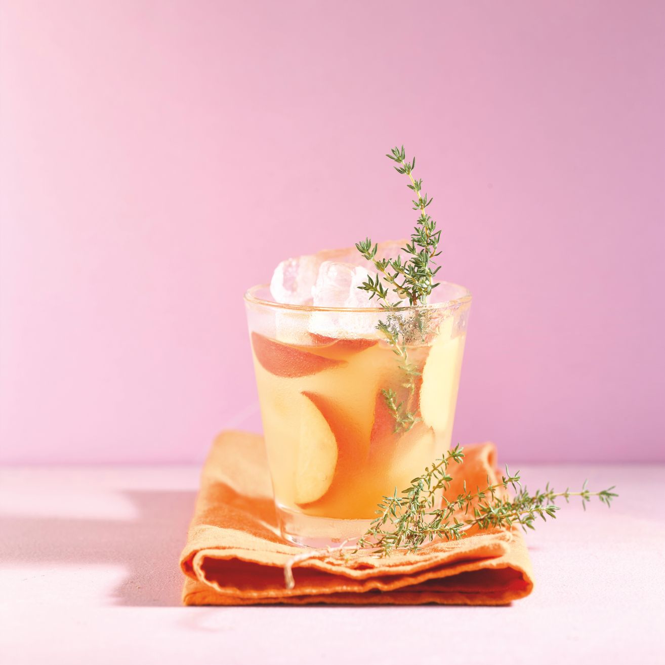 Eistee mit Früchten und Kräutern in einem Glas mit Eiswürfeln.